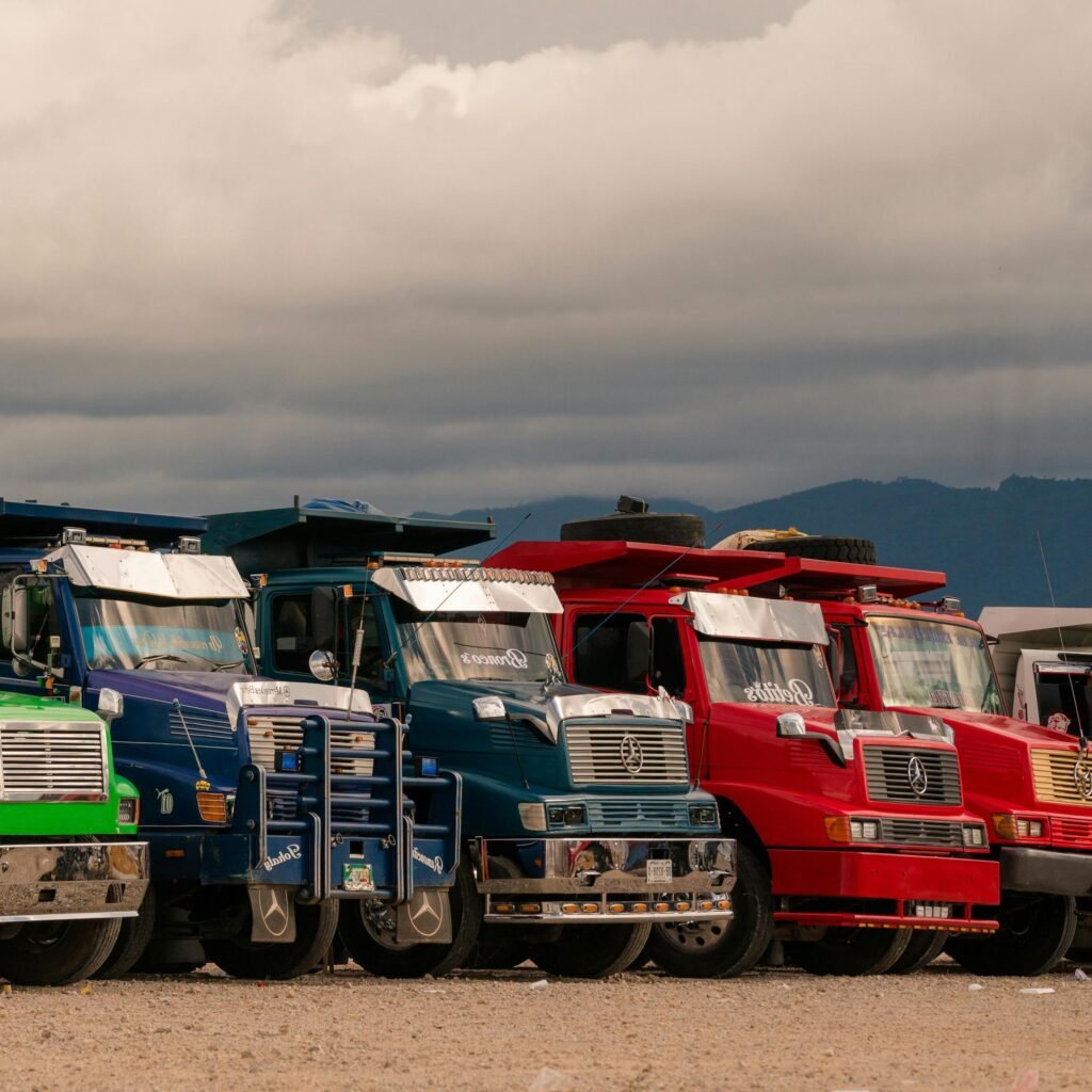 A lineup of vibrant trucks parked outdoors beneath cloudy skies, showcasing diversity in vehicle colors.